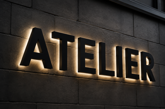 Illustration IA : Lettres noires ATELIER avec un halo lumineux chaud sur un mur gris.